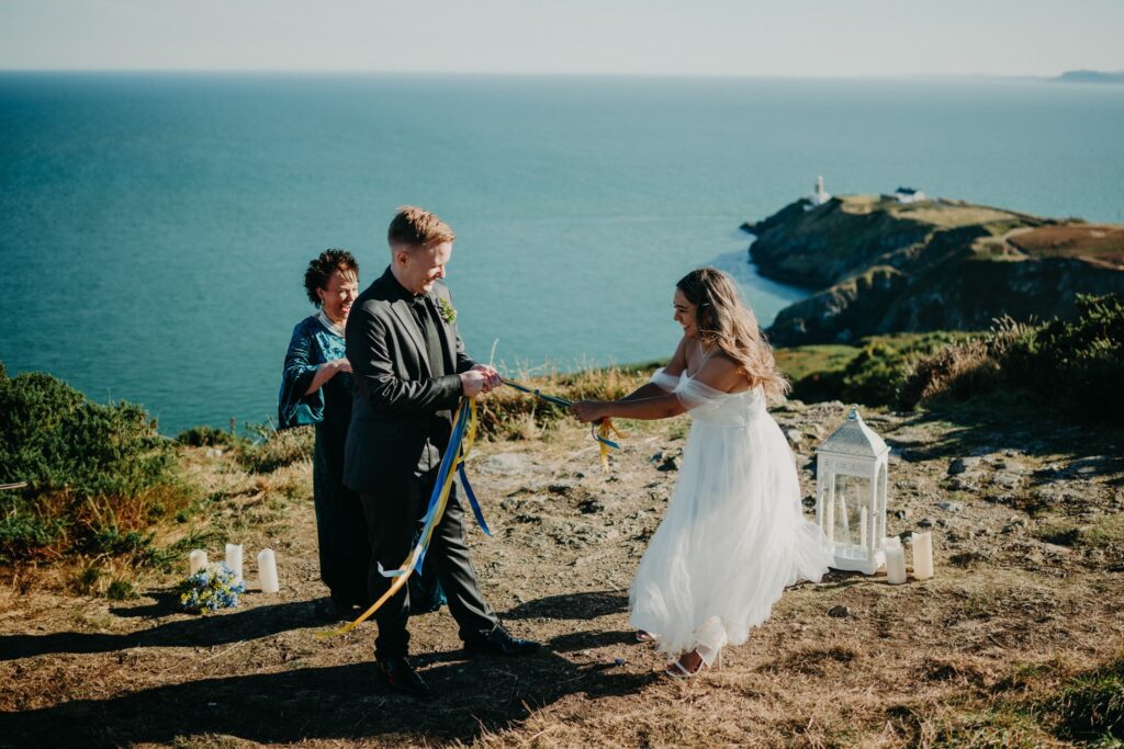 Couple taking part in a Celtic handfasting ceremony during their Ireland elopement on dramatic coastal cliffs overlooking the ocean