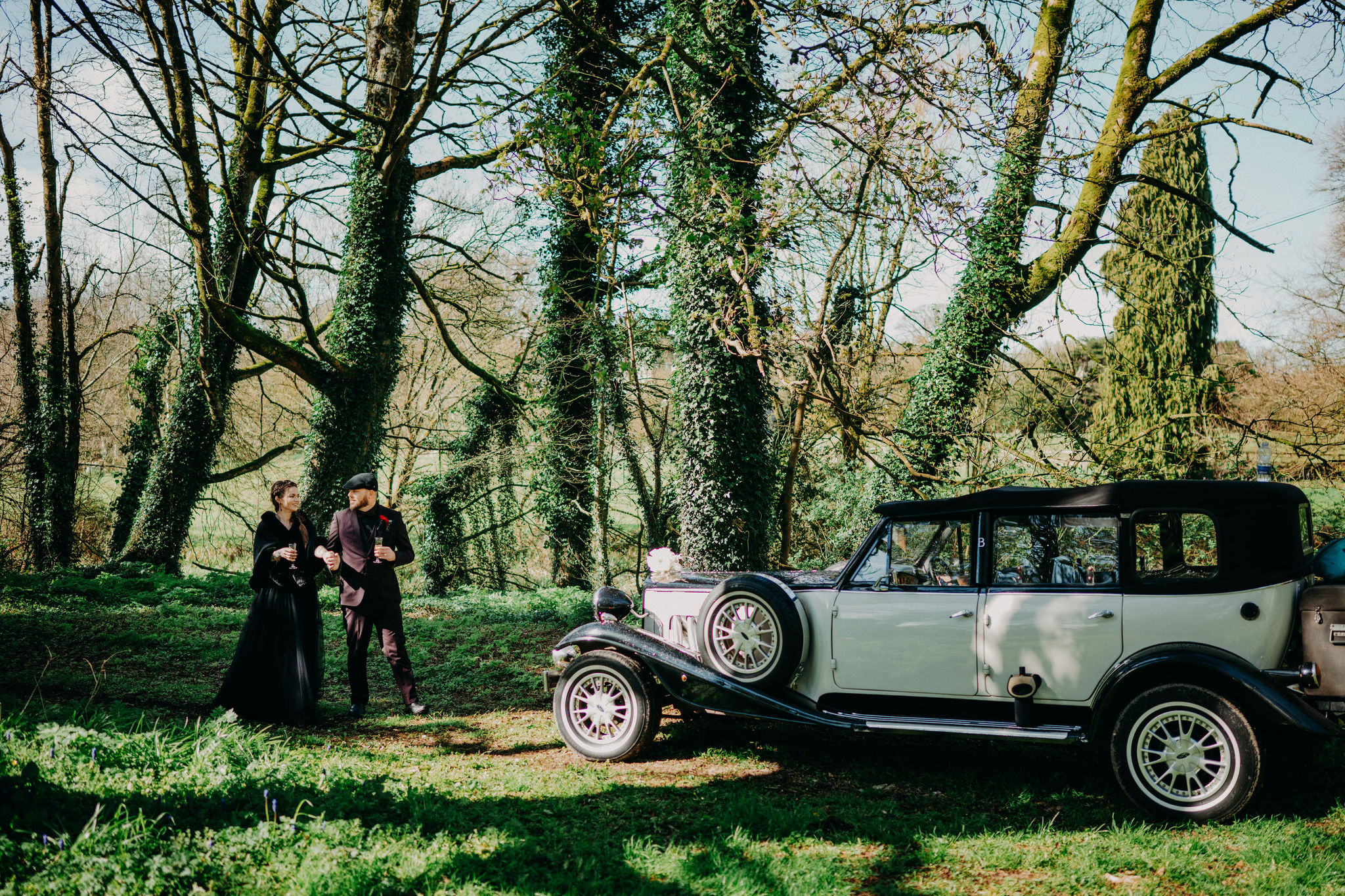 Couple walking beside a vintage wedding car in a woodland setting during their Ireland elopement