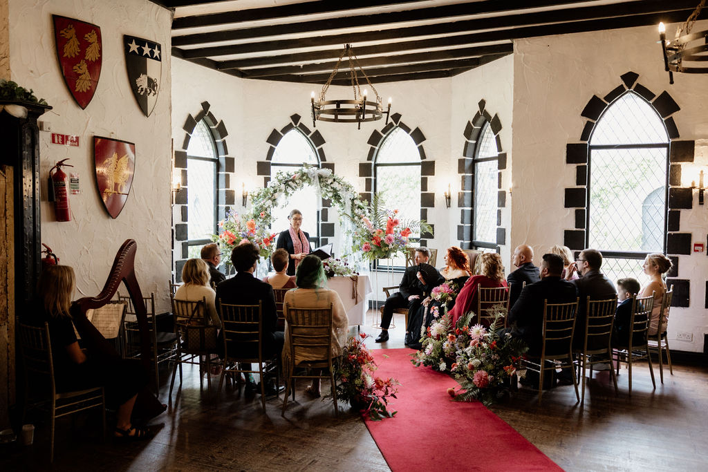 Intimate wedding ceremony inside Kinnitty Castle in Ireland with guests gathered around a floral altar beneath gothic-style windows.