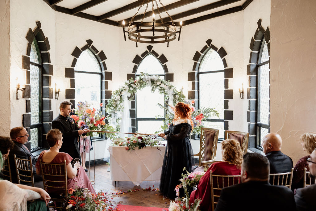 Couple taking part in a handfasting ceremony inside Kinnitty Castle in Ireland surrounded by family and friends.