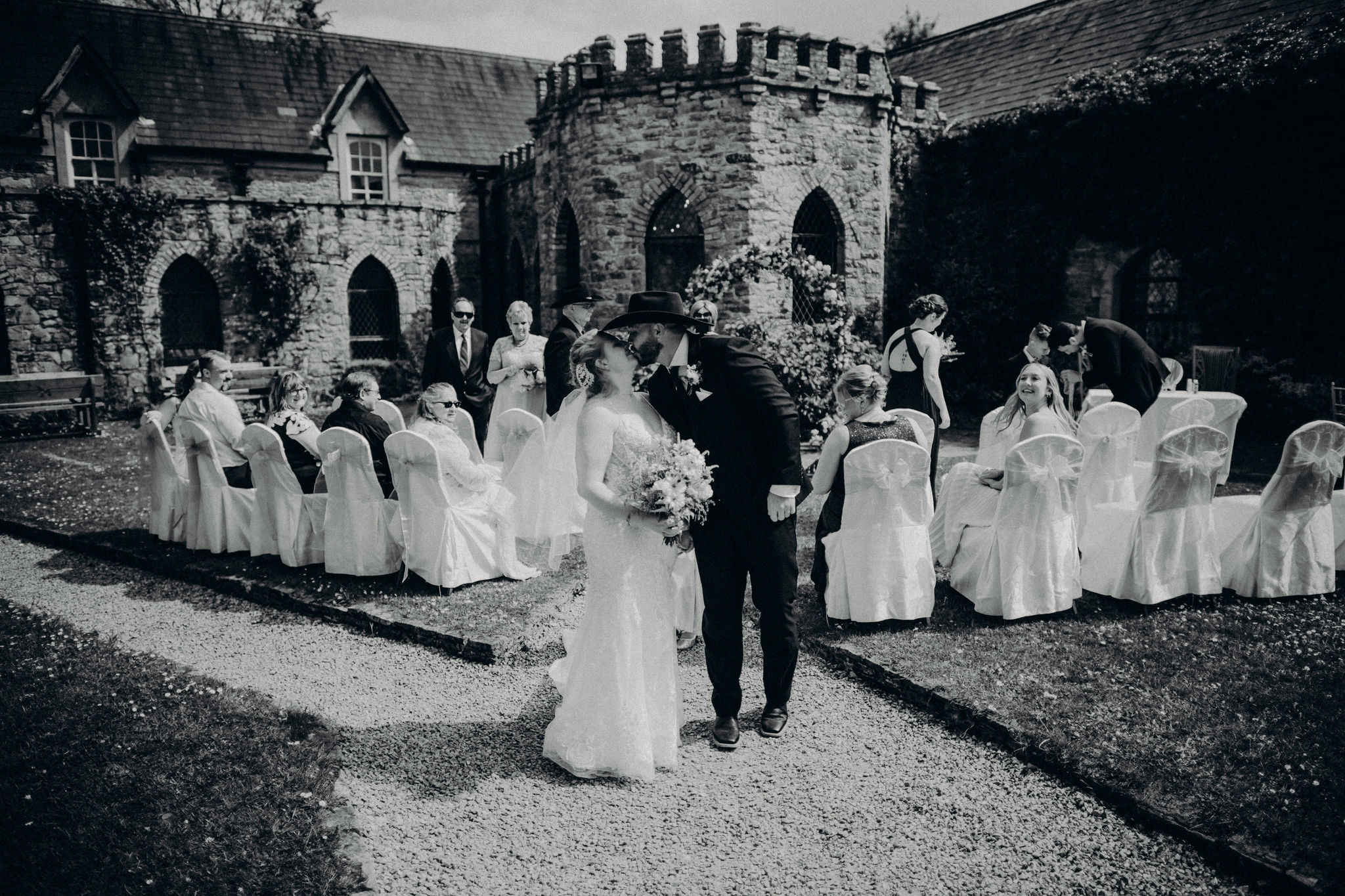 Black and white photo of a bride and groom kissing during an outdoor wedding celebration at Kinnitty Castle in Ireland surrounded by guests.