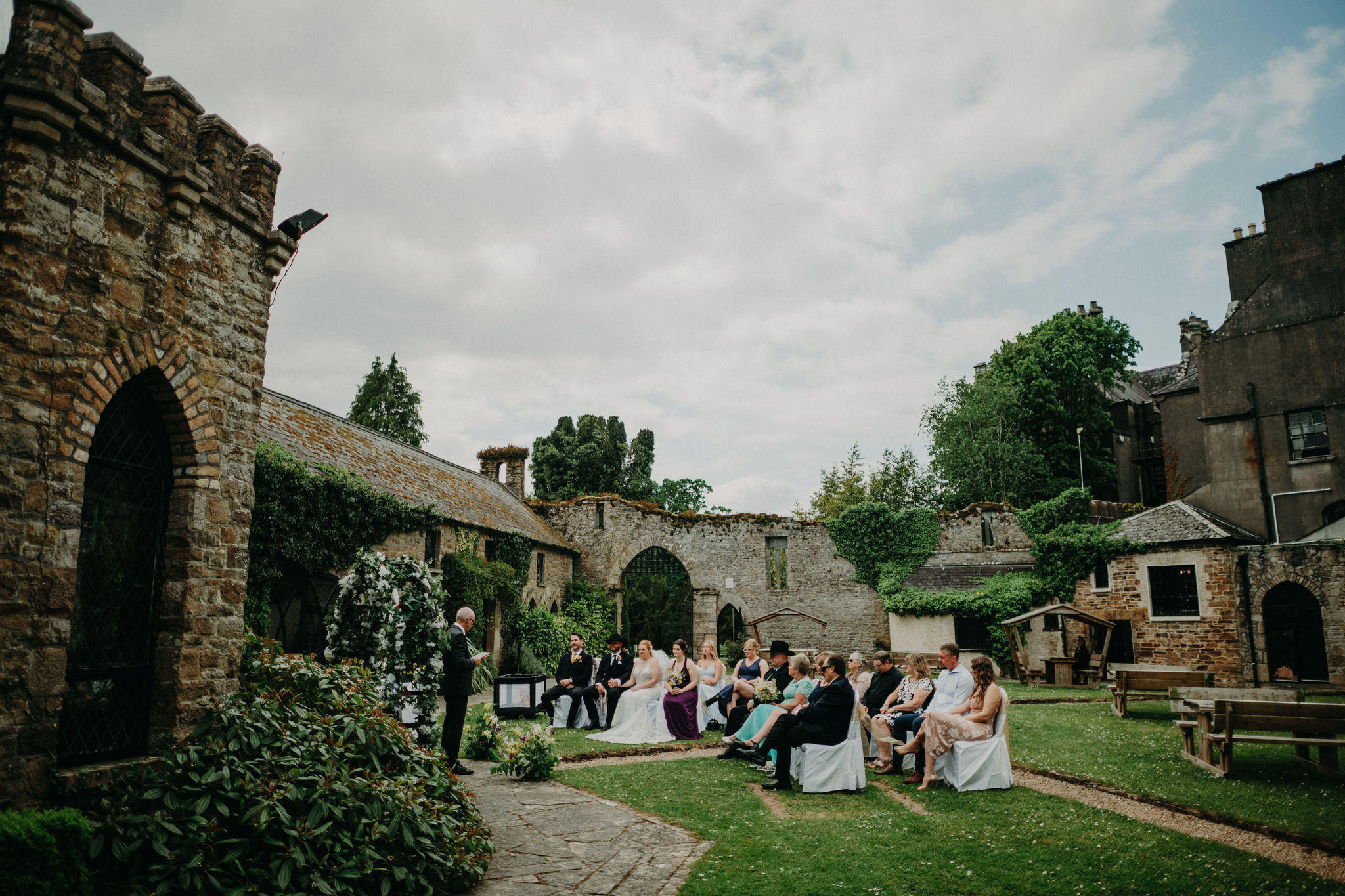 Outdoor wedding ceremony taking place in the historic courtyard gardens of Kinnitty Castle in Ireland.