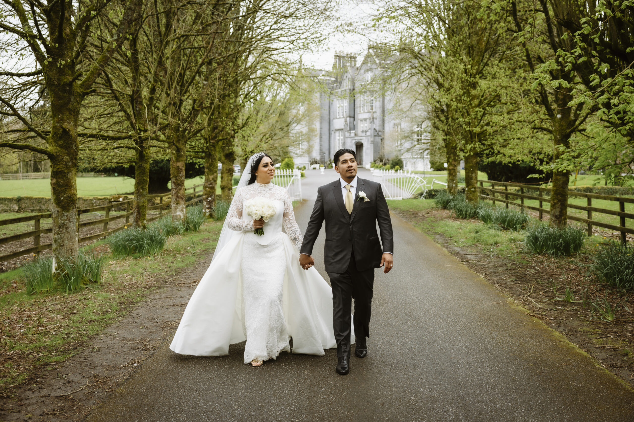 Bride and groom walking hand in hand along the tree-lined driveway at Kinnitty Castle in Ireland.