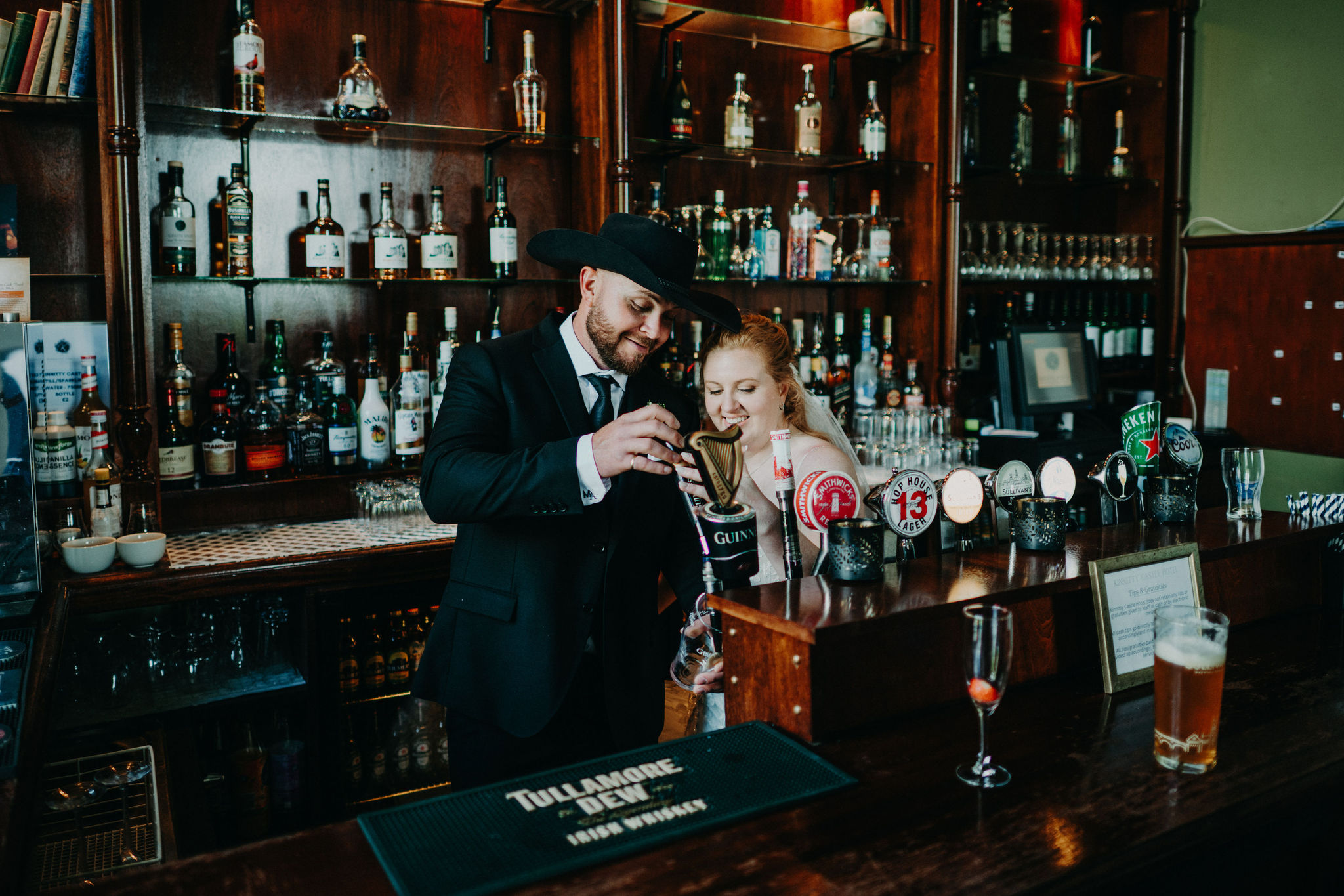Newlywed couple pouring a pint of Guinness together during a pub celebration at Kinnitty Castle in Ireland.