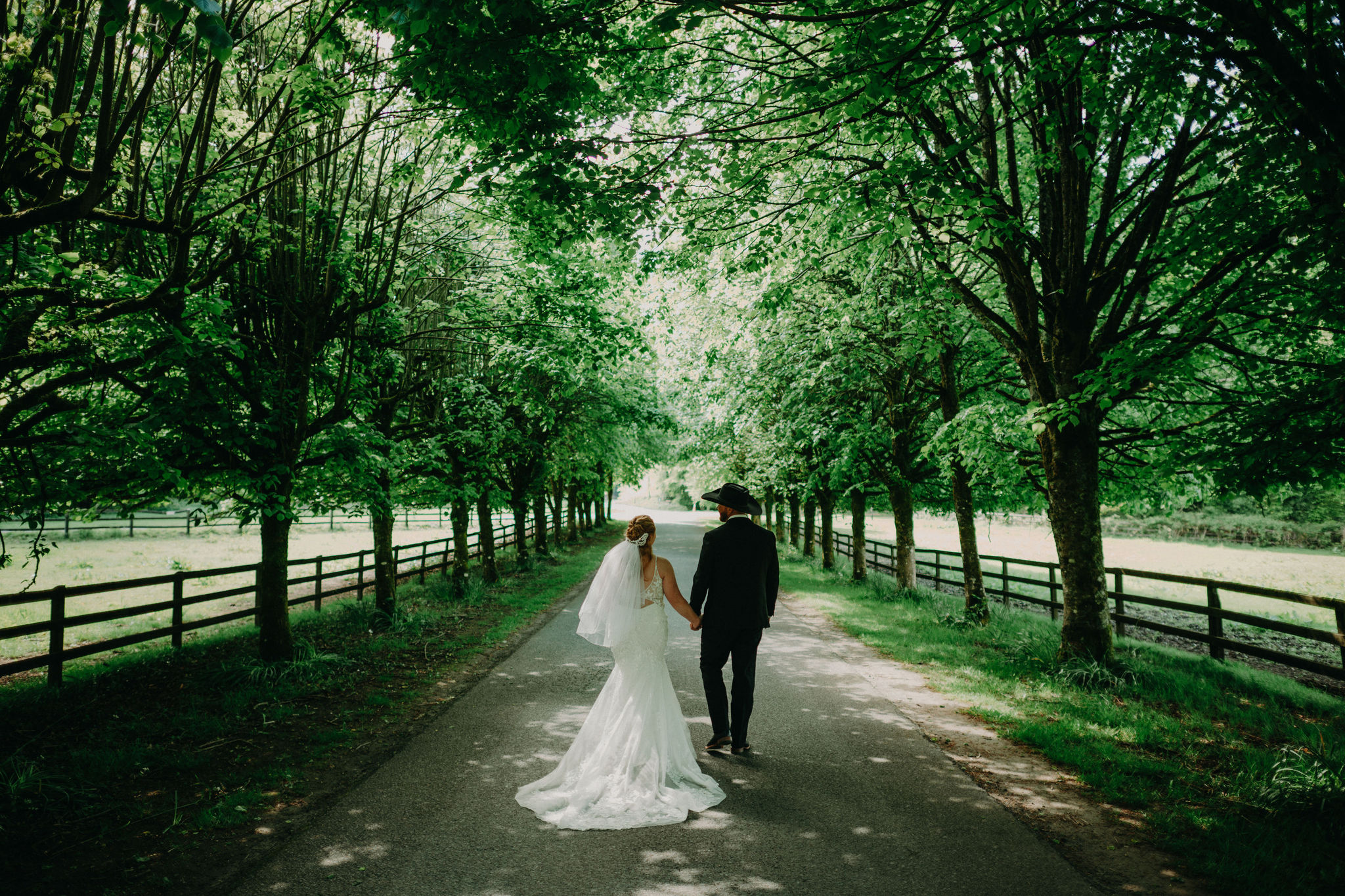Bride and groom walking hand in hand beneath a tree-lined avenue at Kinnitty Castle in Ireland.
