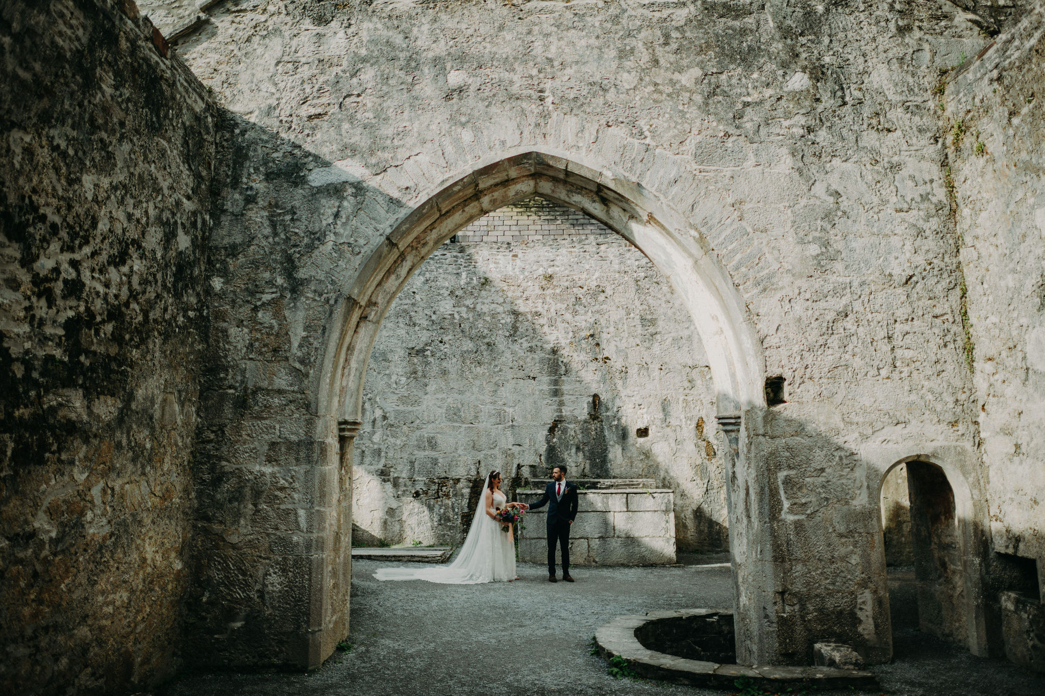 Bride and groom standing beneath stone arch inside Muckross Abbey