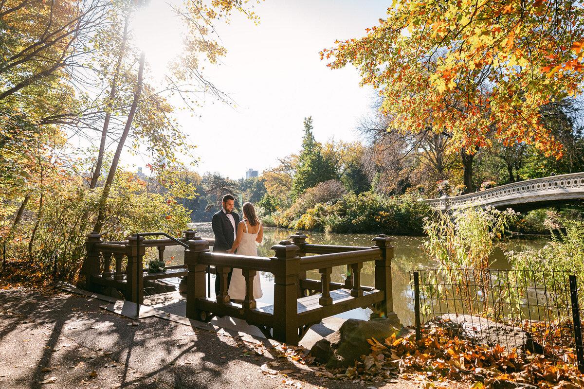 Couple eloping beside Bow Bridge lake in Central Park during autumn in New York City