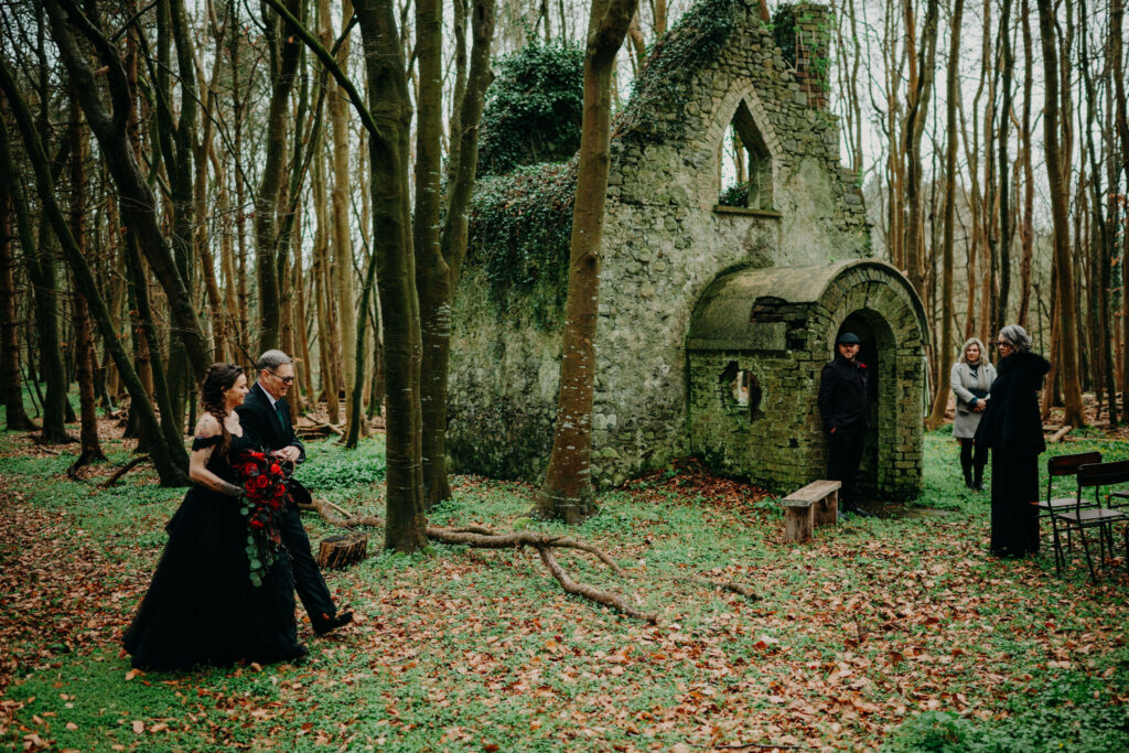 Bride walking through a woodland chapel ruin in Ireland with a bouquet during an intimate elopement ceremony.