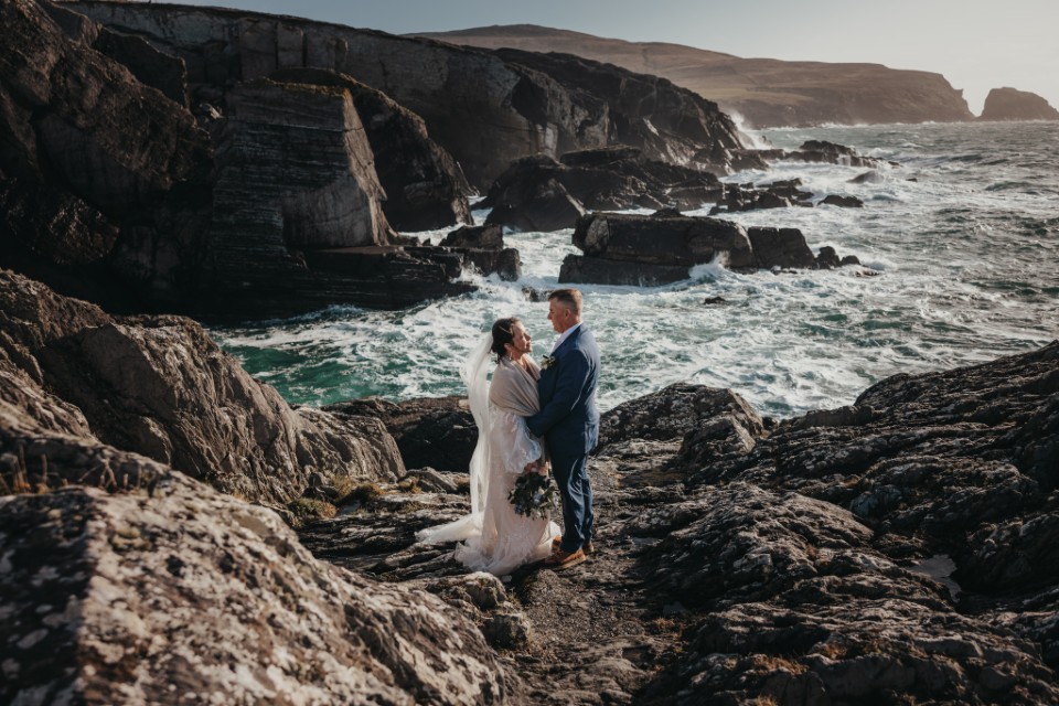Romantic Ireland elopement photos on rugged ocean cliffs with waves crashing along the coastline.