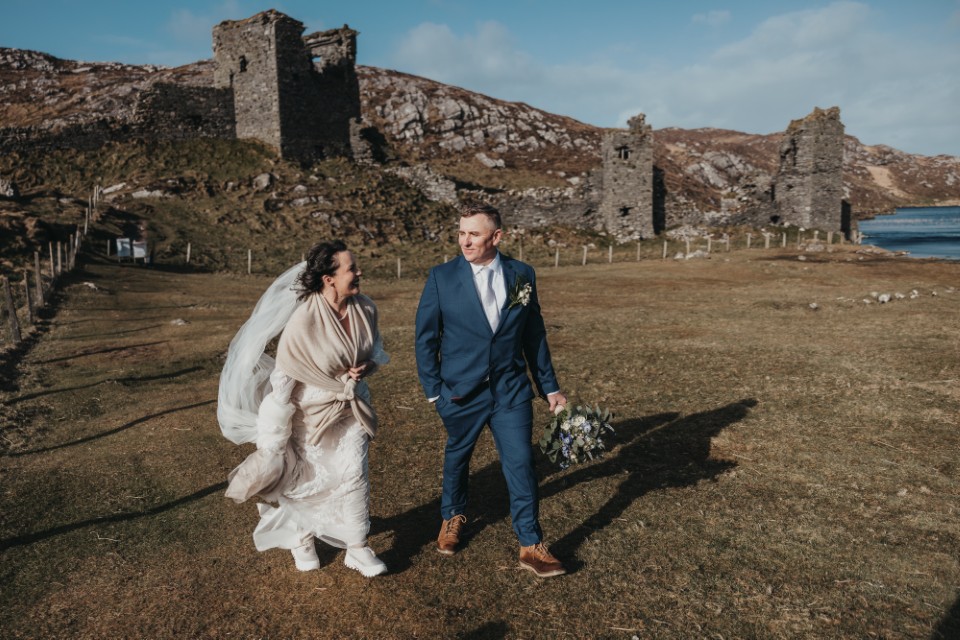 Destination wedding couple walking near ancient ruins in Ireland surrounded by wild landscapes.