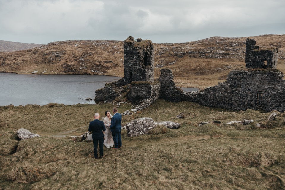Intimate wedding ceremony at ancient Irish ruins overlooking a remote lakeside landscape.