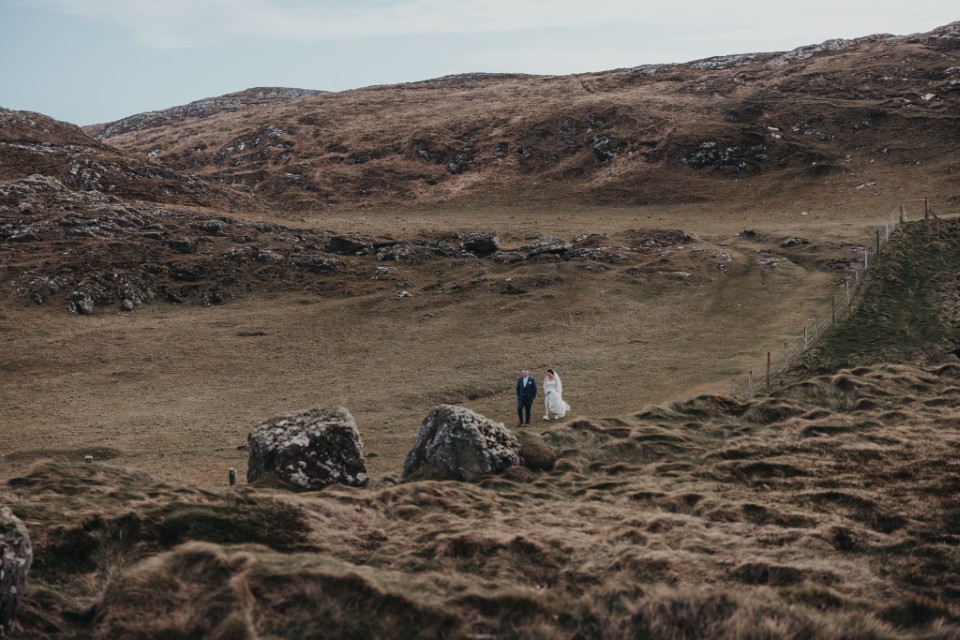 Eloping couple walking through wild scenic Irish countryside after their ceremony.
