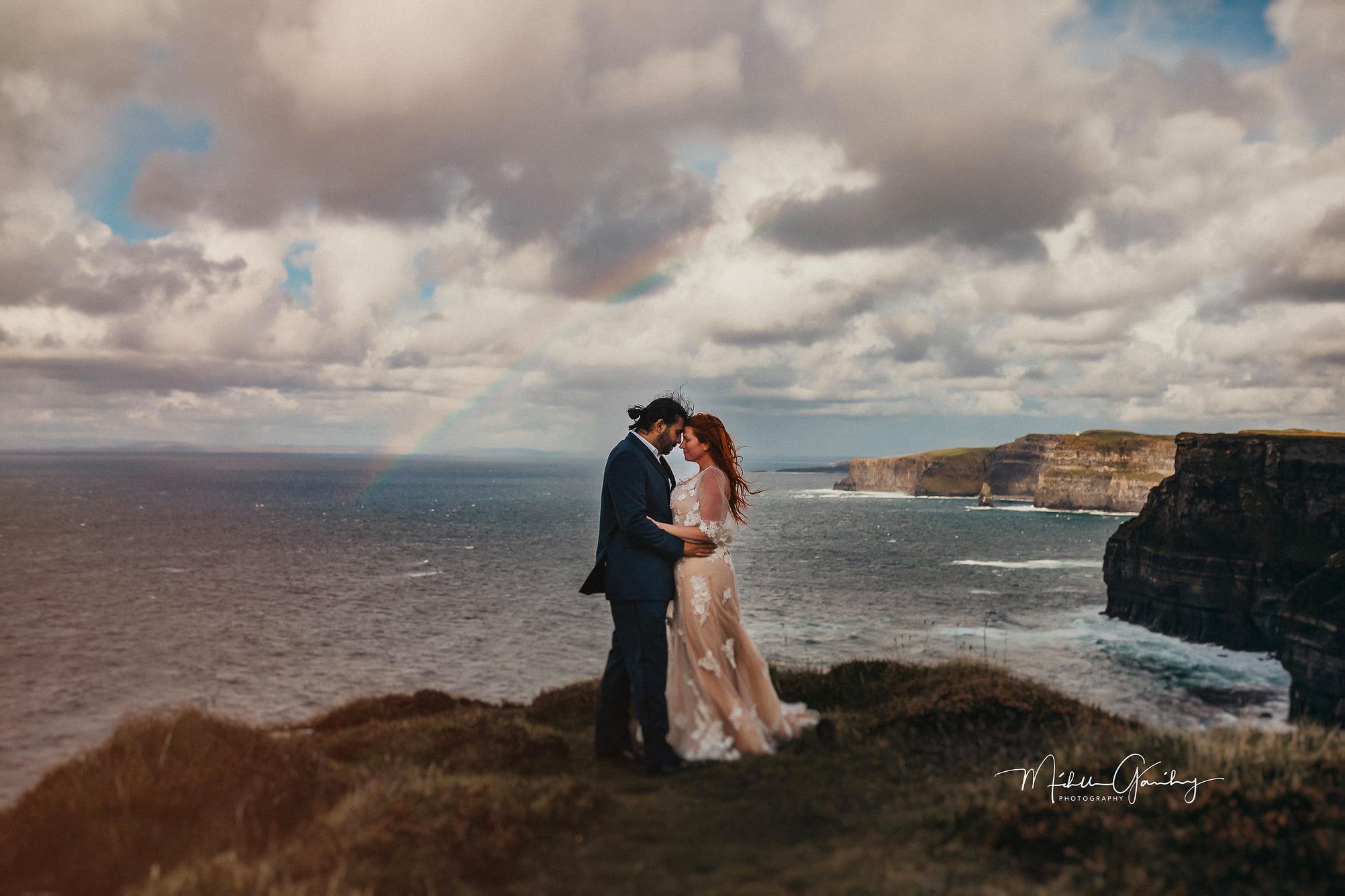 Couple getting married at the Cliffs of Moher in Ireland with a rainbow over the Atlantic Ocean